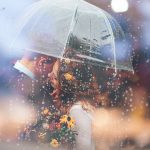 A bride and groom kiss in the rain under an umbrella