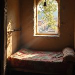 The soft glow of dawn spills through a small, wooden window in a humble bedroom, illuminating the rough-hewn walls and faded patchwork quilts on a thin mattress. Outside, the streets of Florence awaken with the bustling sounds of merchants and children's laughter. The camera focuses on the swaying branches of a nearby olive tree, framing the vibrant rooftops bathed in golden morning light.
