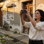 Portuguese woman holding up her smartphone to film an ornate but neglected building facade in Lisbon
